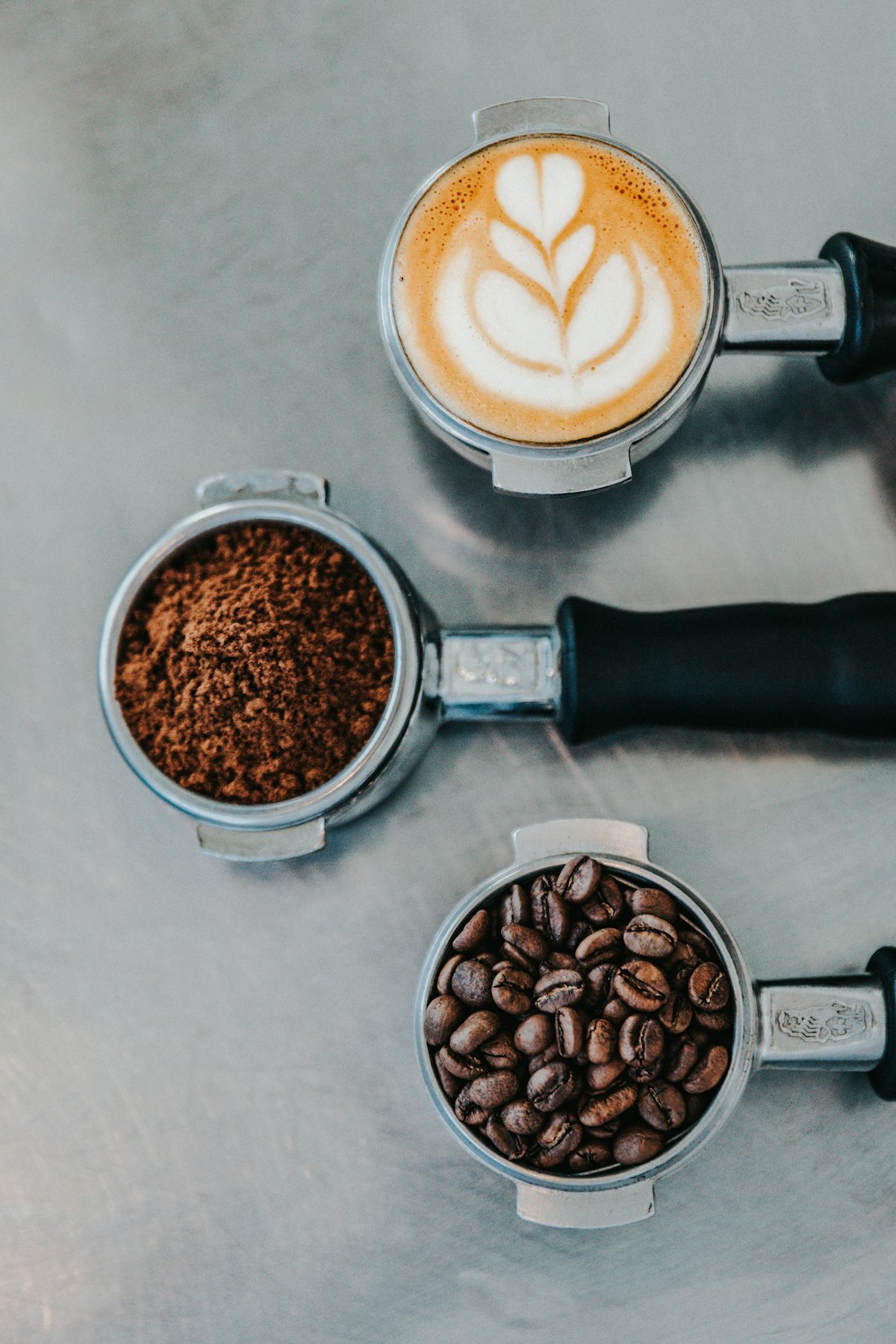 Three espresso portafilters holding latte art, ground coffee, and whole beans
