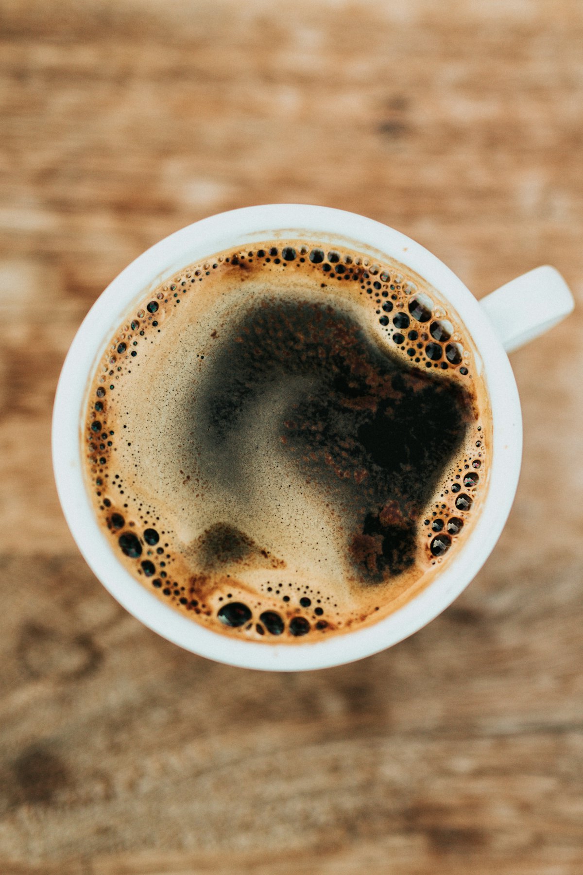 A cup of black coffee seen from above on a rustic wooden table